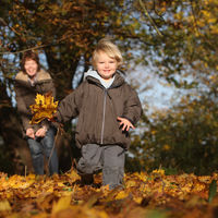 Bild vergrößern: EIne Mutter spielt mit ihren Kindern im Herbst in einem Park